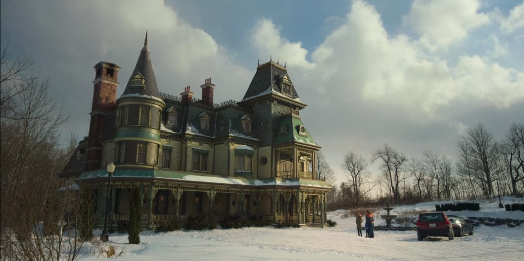 Image from the show Locke and Key. A wide shot of a family standing outside a Gothic mansion in the snow.