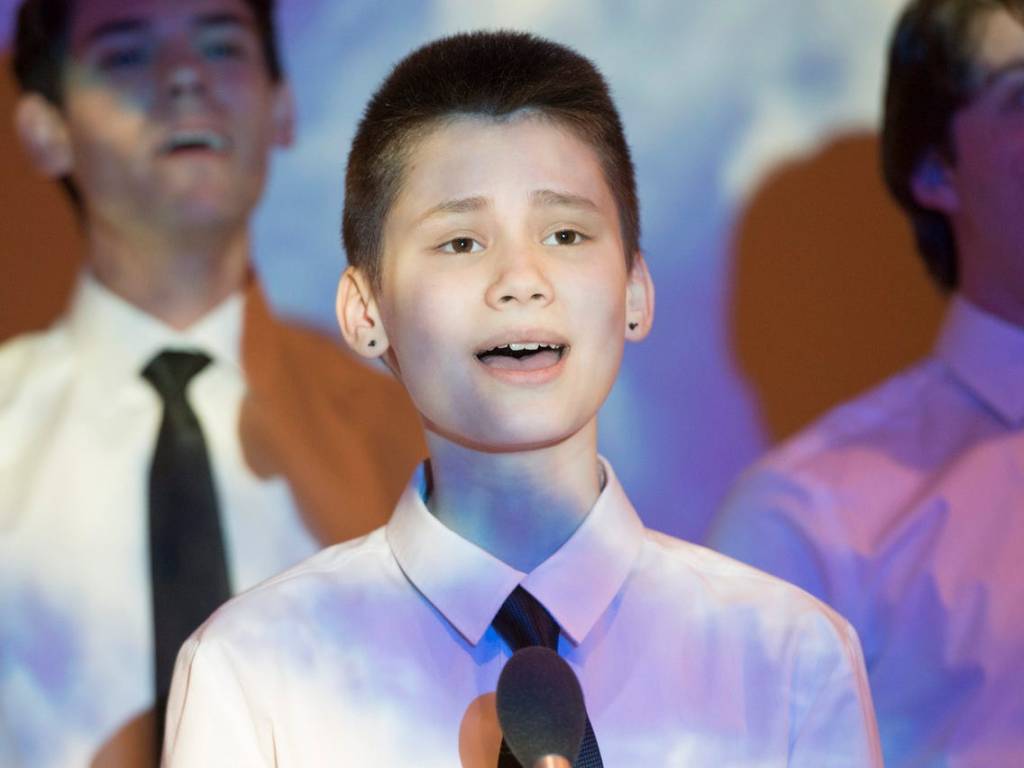 A close up of Buck, who is singing in a choir. He is wearing a shirt and tie.