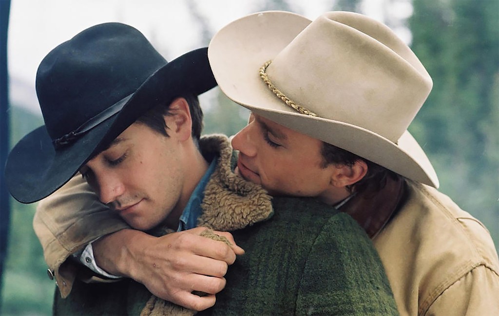 Two men wearing cowboy hands engage in an embrace, with one wrapping his arm around the other.