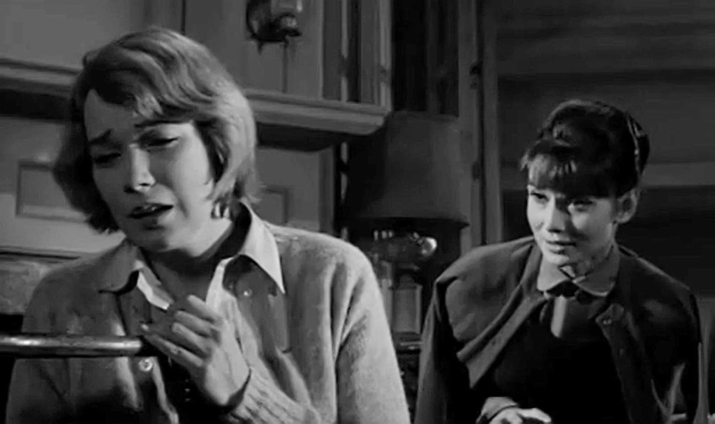 On the left, a blonde woman looks upset. Behind her, another woman tries to console her. The image is in black and white.