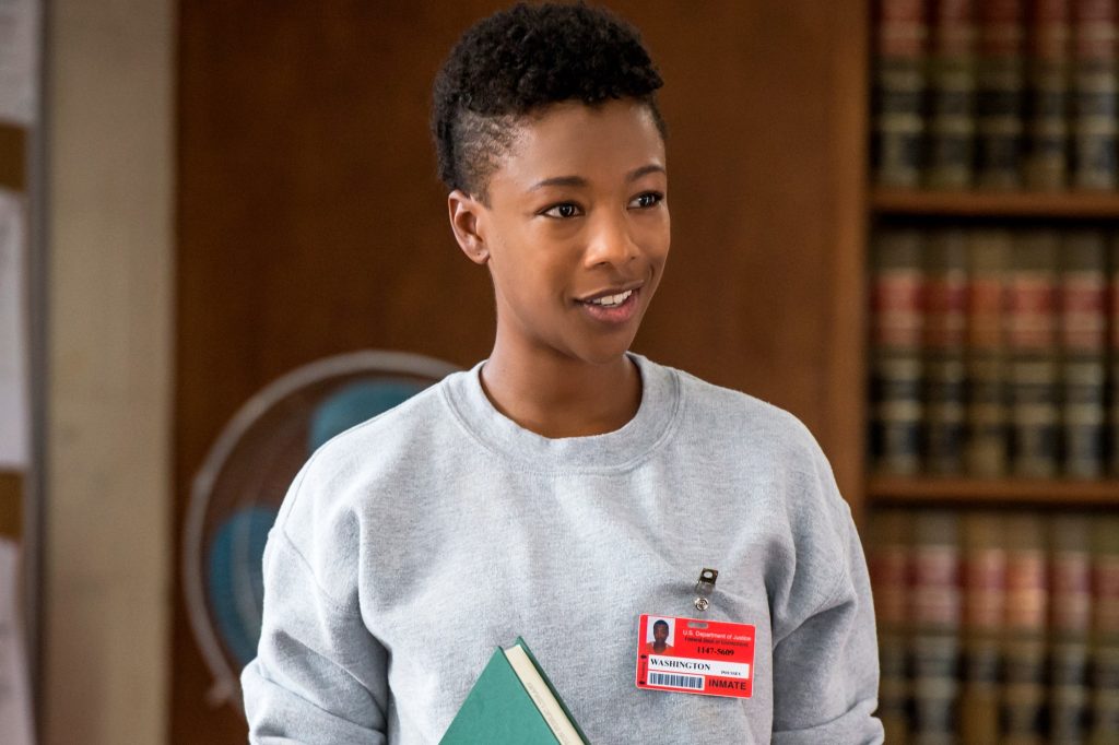 Poussey is holding a book. She is wearing a great jumper and an orange tag with her name on it.