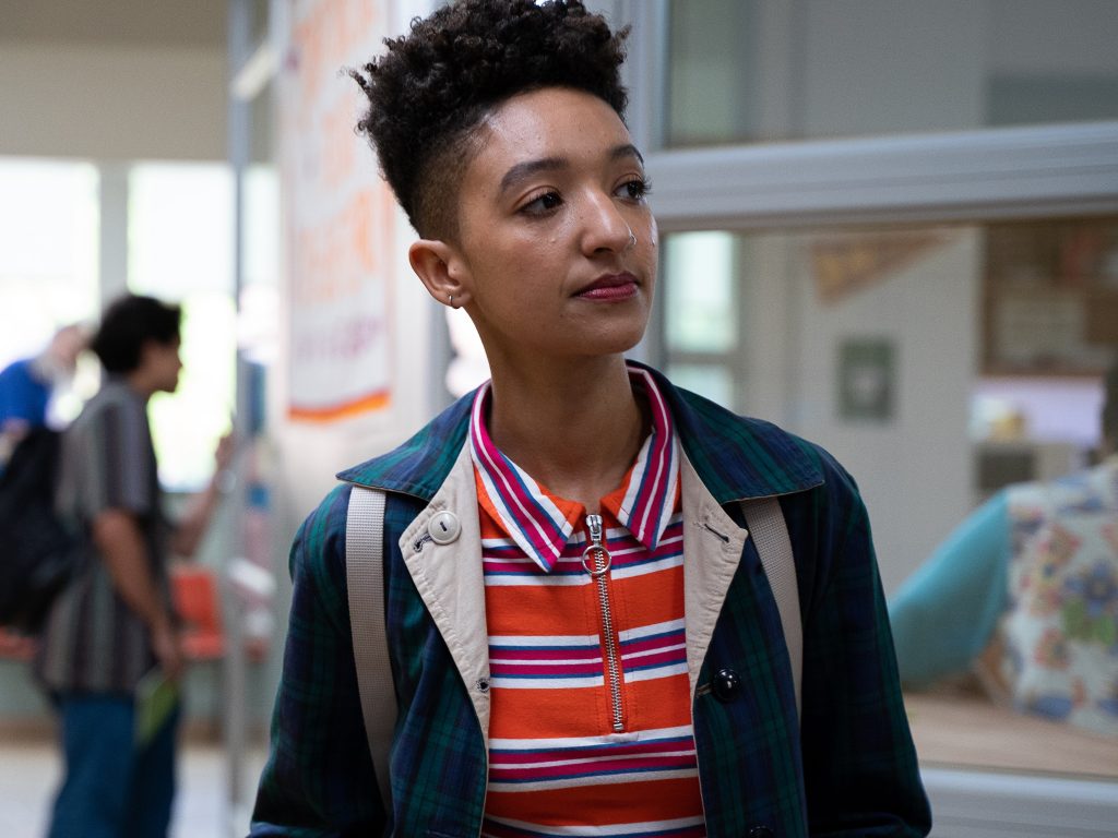 A mid-shot of Ola. She is wearing a dark green coat and orange-striped polo shirt.