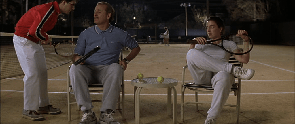 Screencapture from Rushmore. A man and a woman sit next to a tennis court and a teenager is talkign to the man. 