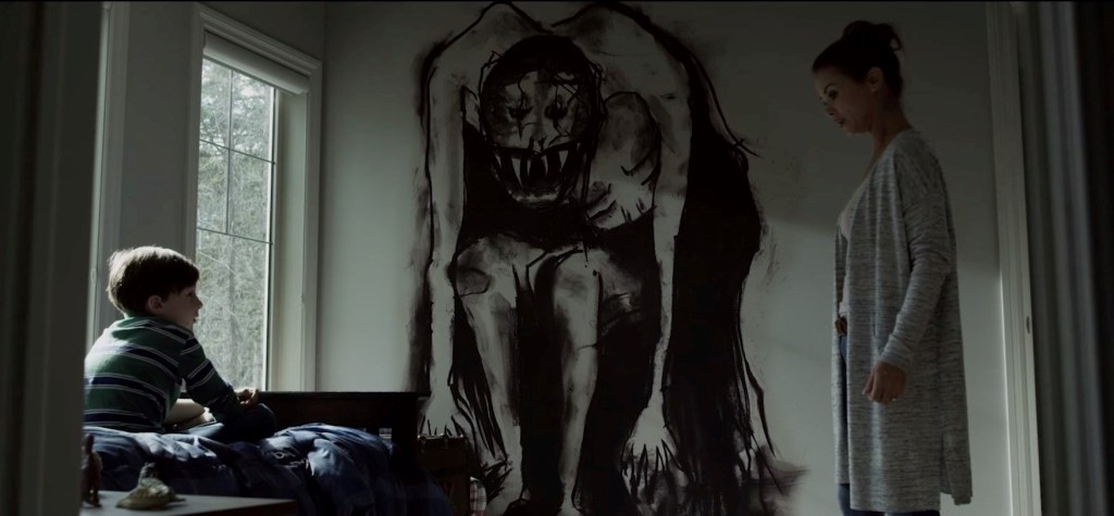An image from the horror film Z. A woman and son look at each other across the room, and in the middle is a monster painted on the wall.