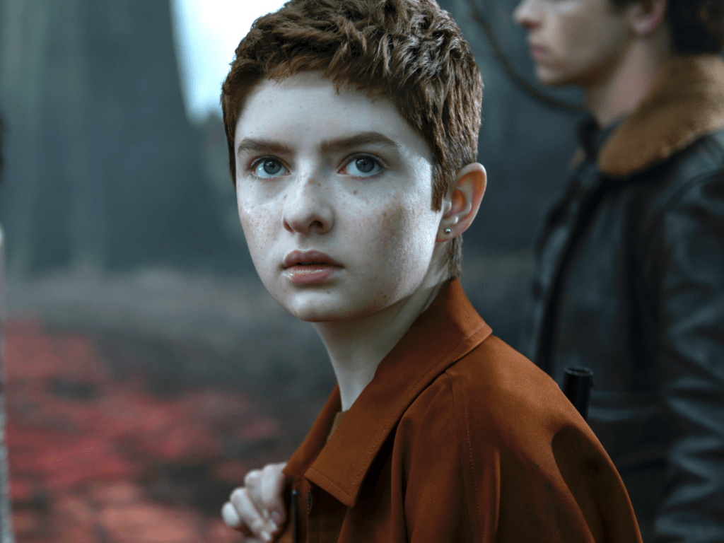 Theo looks up as he walks. He is wearing a burnt orange jacket.