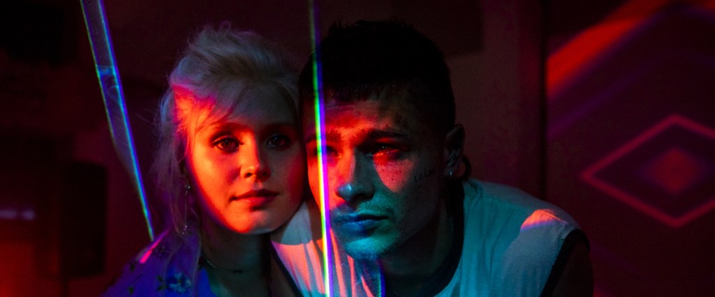 The image is from the film Babyteeth. Milla and Moses stand close to one another in a red-tinted room covered with lasers.