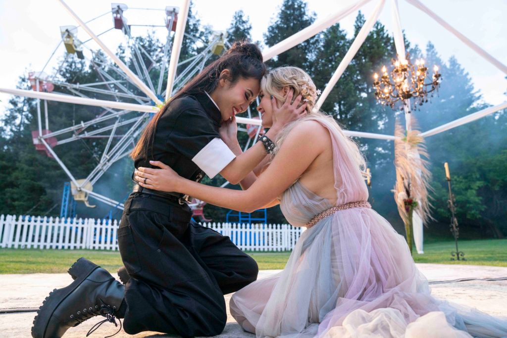 Karolina and Nico hold one another in am embrace at a fairground. Nico is dressed all in black whilst Karolina wears a pastel coloured dress.