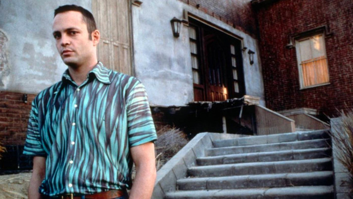 Norman Bates stands outside of a run down house. He looks directly at the camera.