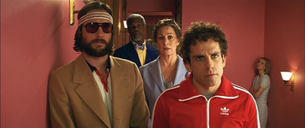 Screencapture from The Royal Tenenbaums. 5 people stand in a hallway. 