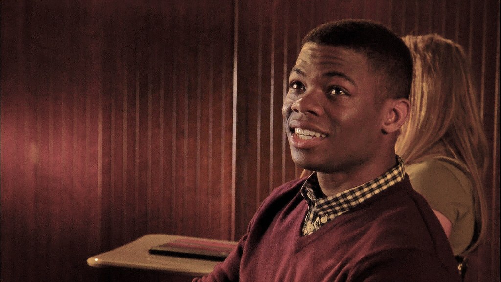 Calvin is sat at a desk. He is half-smiling.