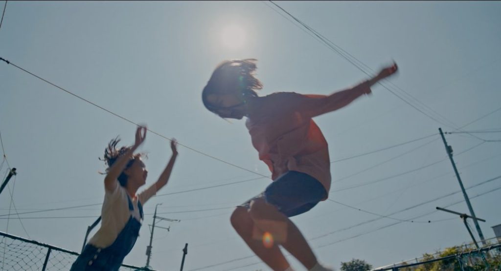 The image is from House of Hummingbird. Two girls jump and play on a summer day.