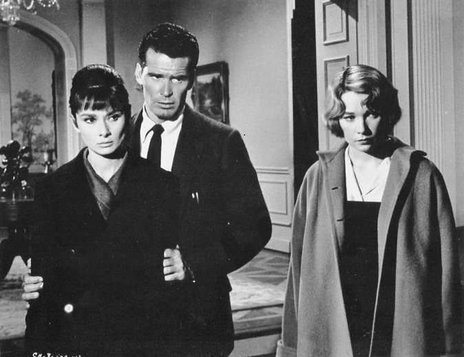 Dr. Joe Cardin [James Garner] stands behind Karen Wright [Audrey Hepburn], holding her firmly by her upper arms. Martha Dobie [Shirley MacLaine] stands to their left. All three have firm and displeased expressions.