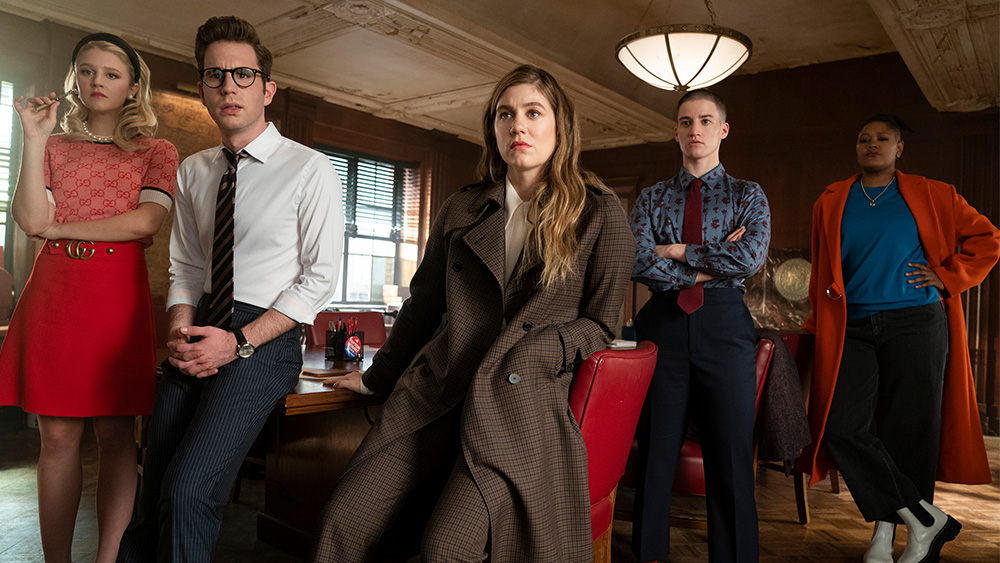 A group of young adults sit in a conference room. All are well-dressed and appear to be staring at something.