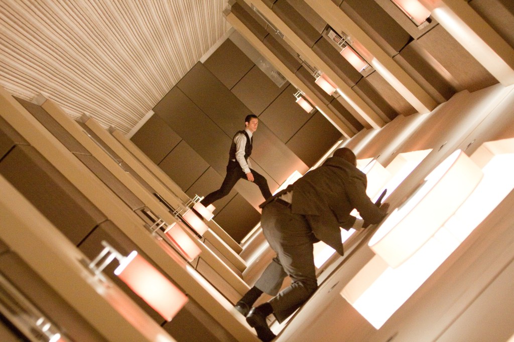 Joseph Gordon-Levitt in a scene from the film 'Inception.' His character is wearing a suit while in a rotating hallway, while a man on the wall watches.