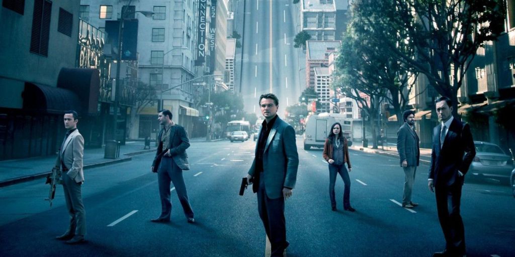 Characters in the film 'Inception' stand on a city street. Behind them, the street curves sharply upwards.
