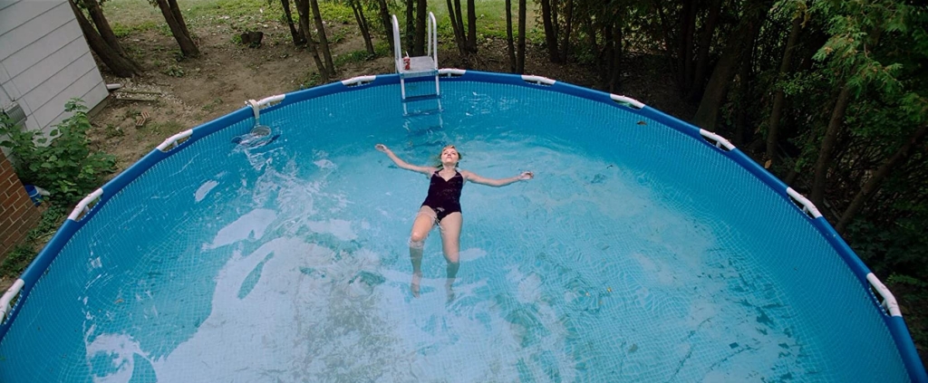 A girl in a black swimsuit lays on her back in a swimming pool.
