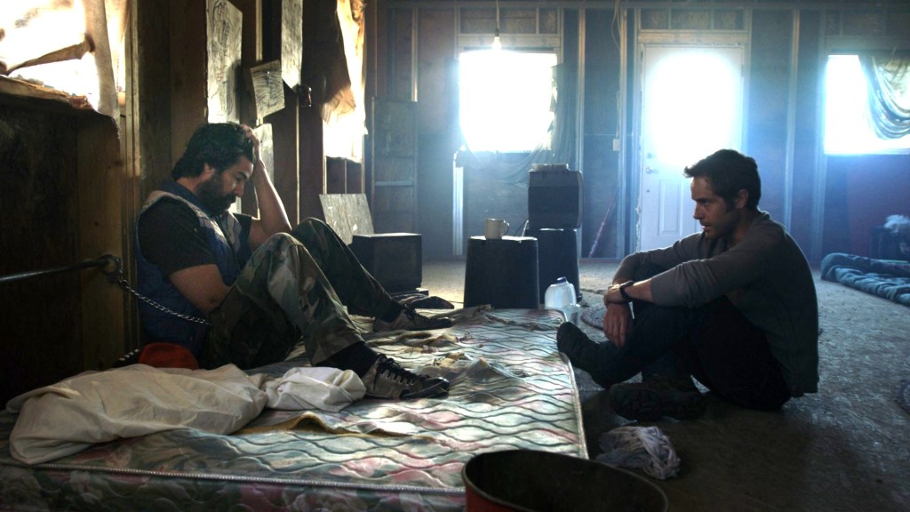 This image is from Resolution. Mike and Chris site opposite one another. One sites on a worn out mattress, the other on the floor. 