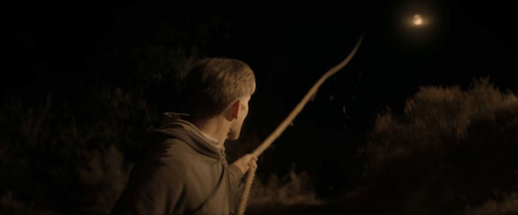 This image is from The Endless. Aaron looks up at a rope that leads up into the night sky and pulls it.