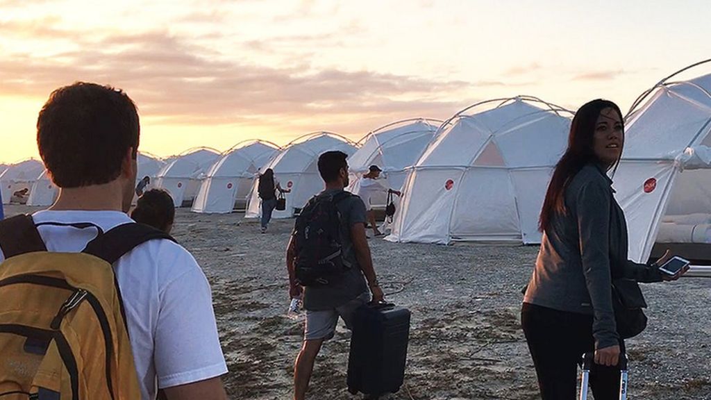 Image from the Netflix film Fyre: The Greatest Party That Never Happened. Influencers attending the festival walk towards a series of domed white tents, looking shocked.