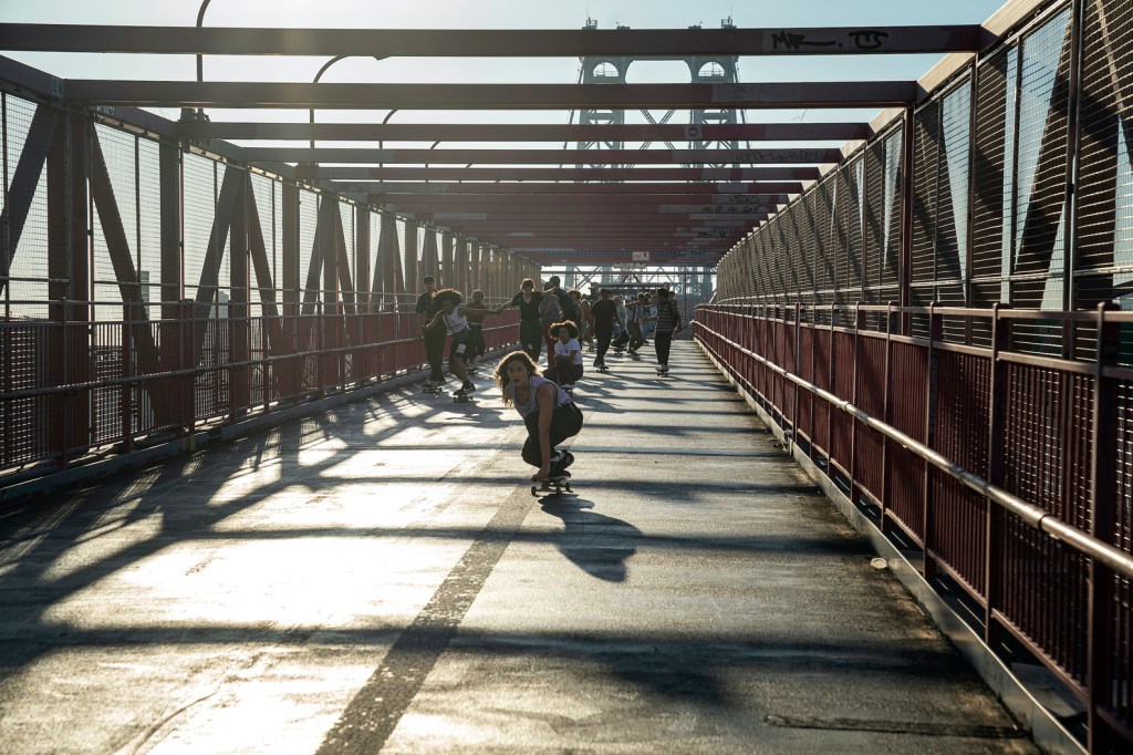 A large group of people skate across a bridge.