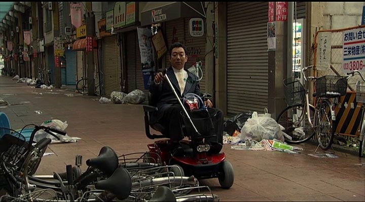 A character moves his mobility scooter through a deserted shopping street in Tokyo