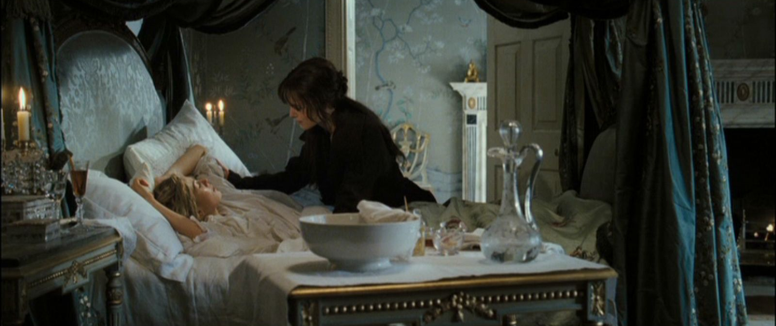 Image from Pride and Prejudice. A woman lies ill on her bed whilst another dressed in black comforts her.