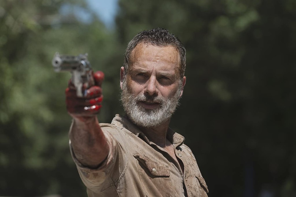Image still from The Walking Dead episode What Comes After. A dishevelled Rick looks into the camera, bloodied hand and pointing his gun.