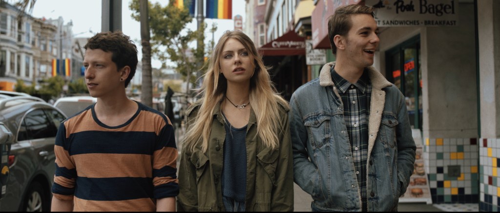 three young adults walk outside in San Francisco, with rainbow pride flags on the lampposts