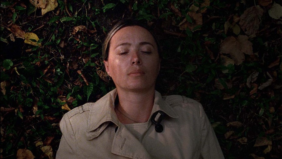 This image is from the film Beginning. A woman lies on the ground with her eyes closed.
