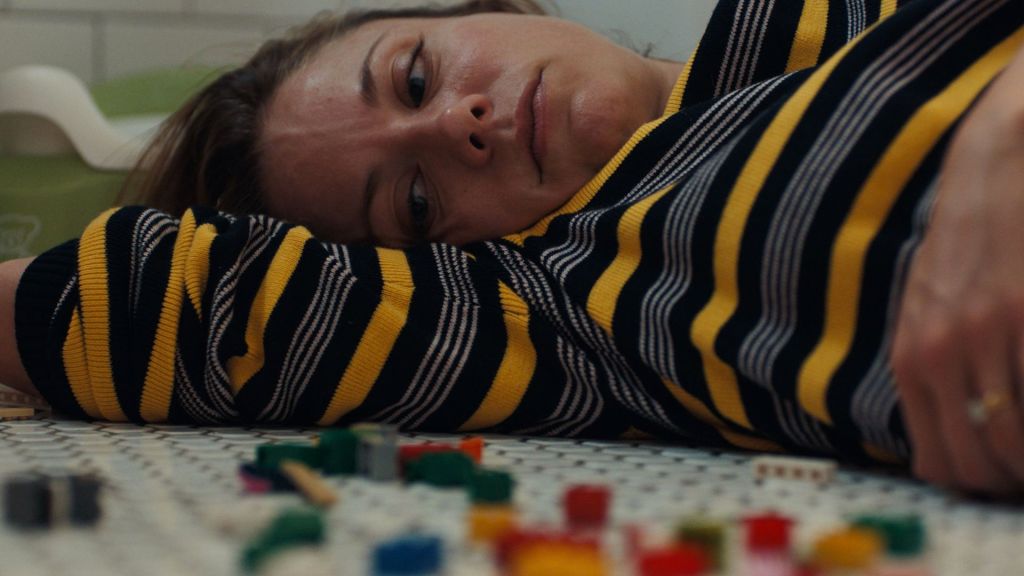 A young adult woman lies on a bathroom floor looking at an assortment of colorful blocks.