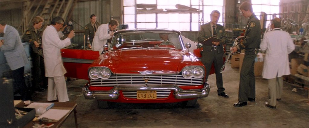 police and examiners in white coats surround a red car with its doors open