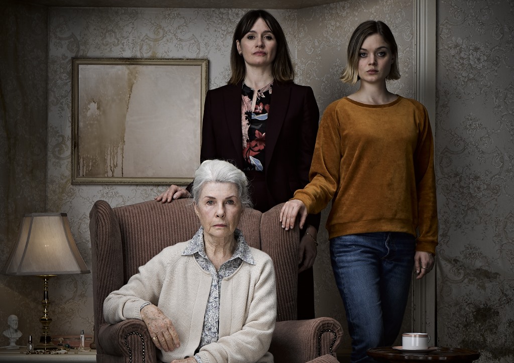 Image from the horror film Relic. Three women pose for a family portrait in a decrepit looking living room, staring into the camera.