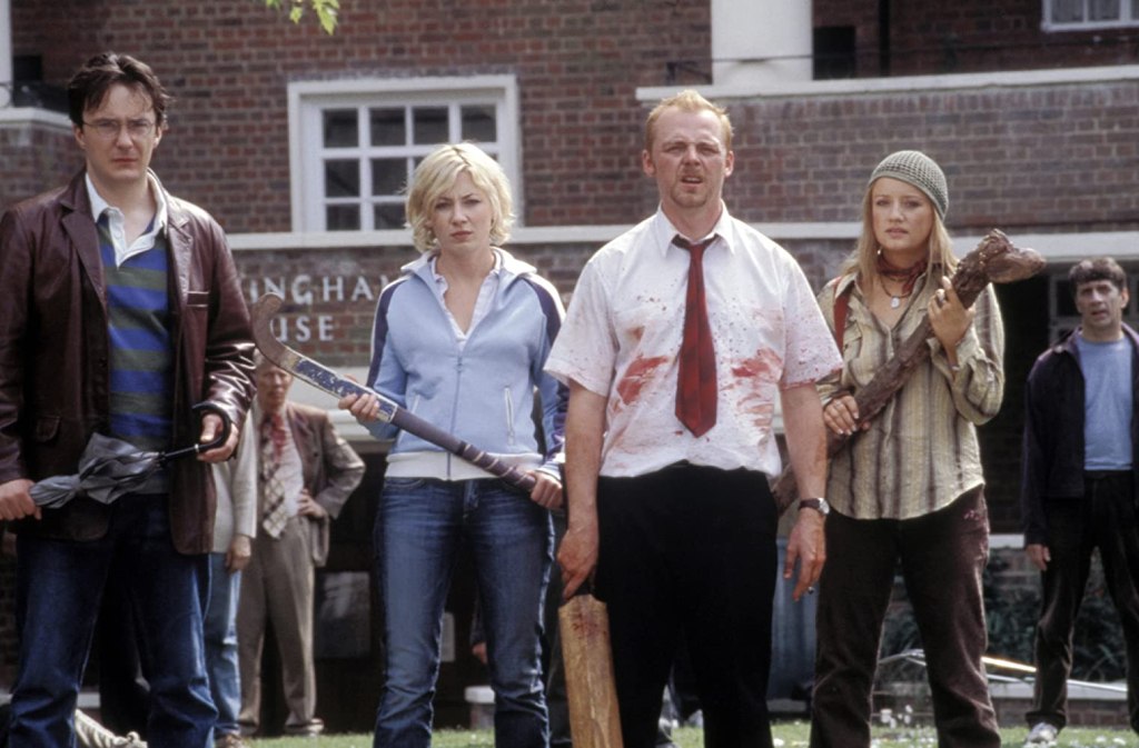 two men and two women stand in a line holding makeshift weapons including an umbrella, hokckey stick, and paddle