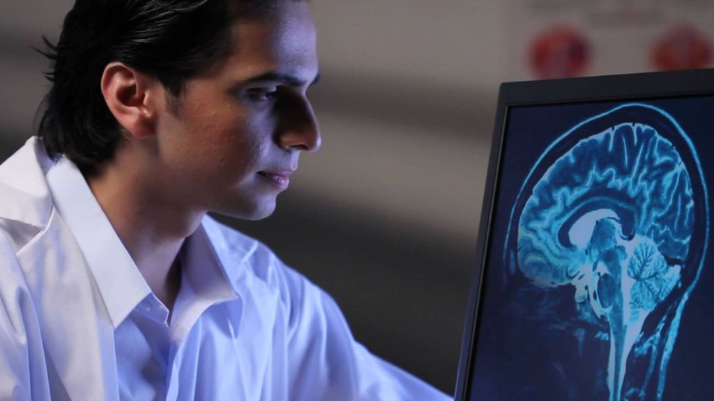 A doctor looks at a screen showing an image of a brain.
