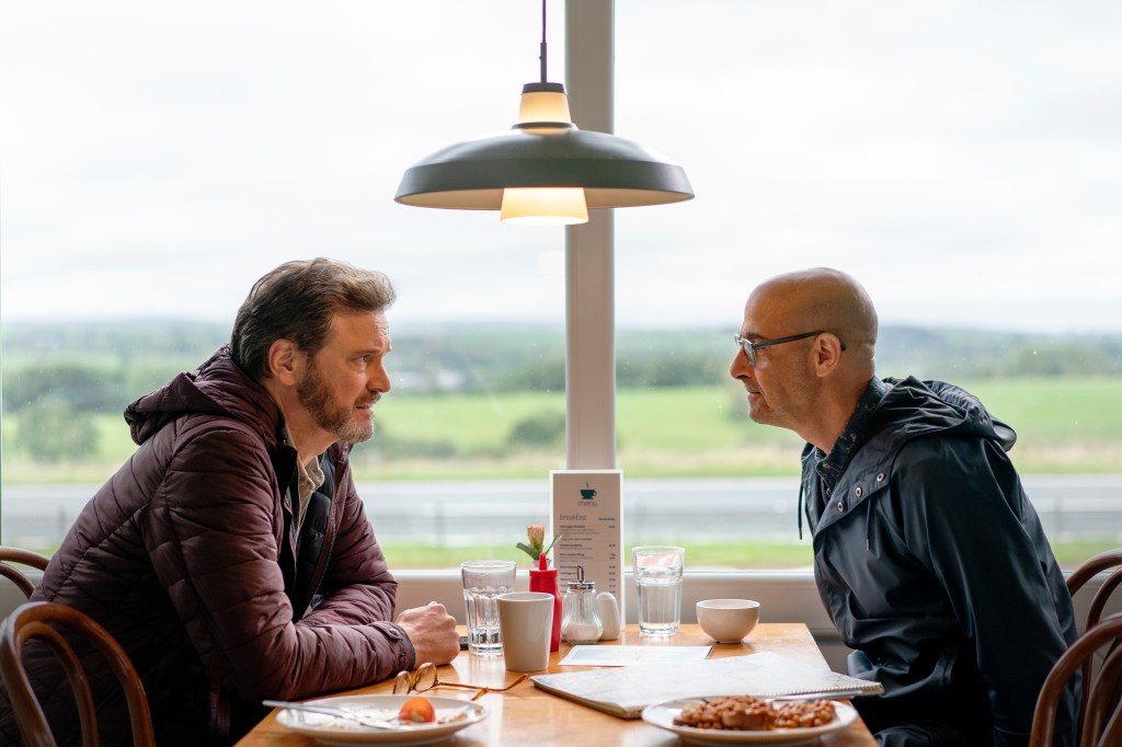 Sam, Colin Firth, and Tusker, Stanley Tucci, sit opposite each other in a British breakfast diner cafe