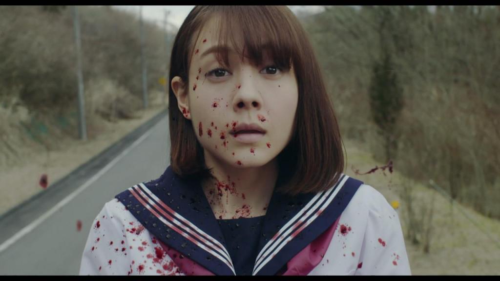 a teenage girl in a blood-splattered school uniform stands on an empty road