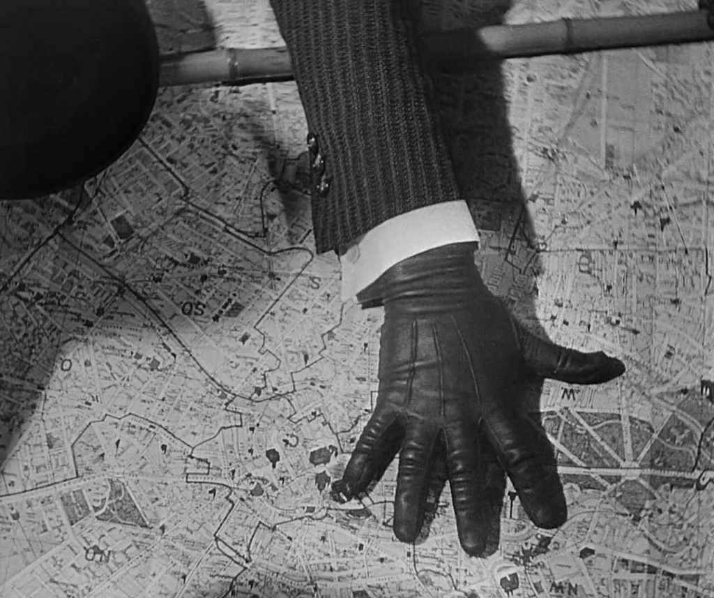 A black, gloved hand appears on top of a map.