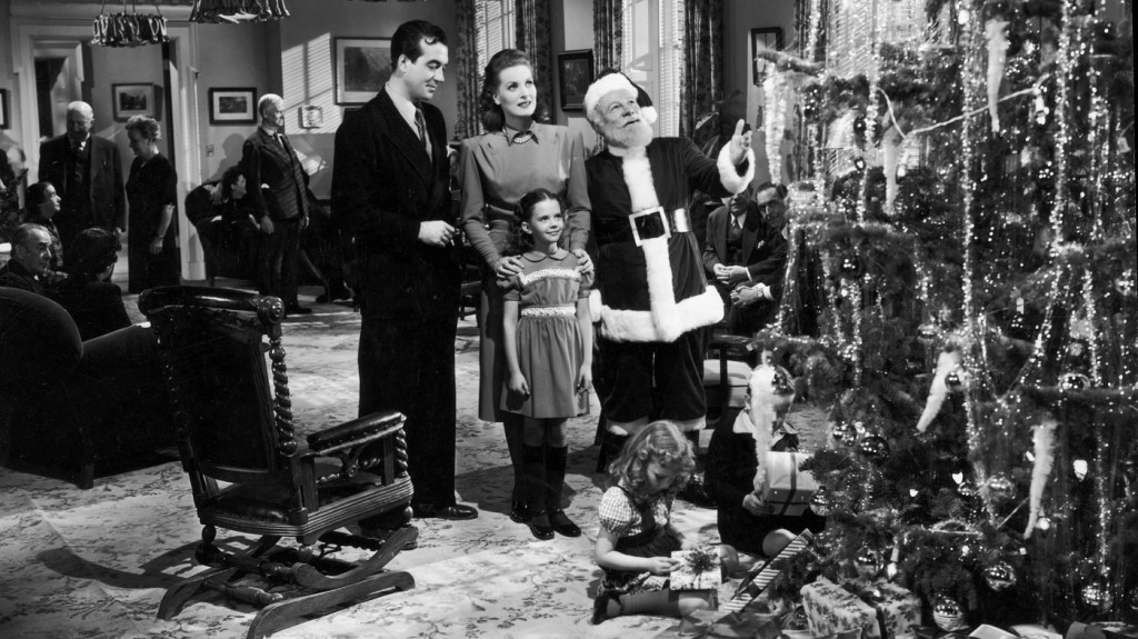 Kris Kringle talks to a man, woman and little girl while looking at a tree.