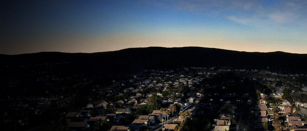 An establishing shot of a light blue sky before sunset overlooking a suburb.