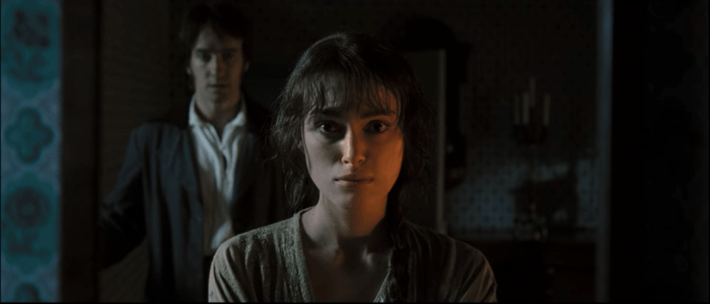 Elizabeth stares in the mirror as Darcy stands behind her, dropping off a letter.