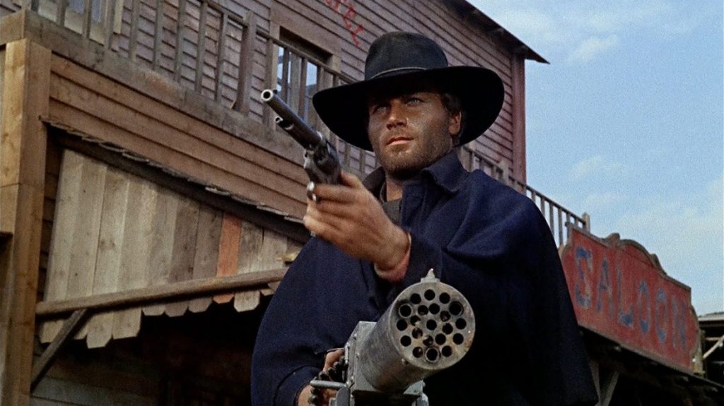 Django (Franco Nero) holds a revolver in one hand and a machine gun in the other.