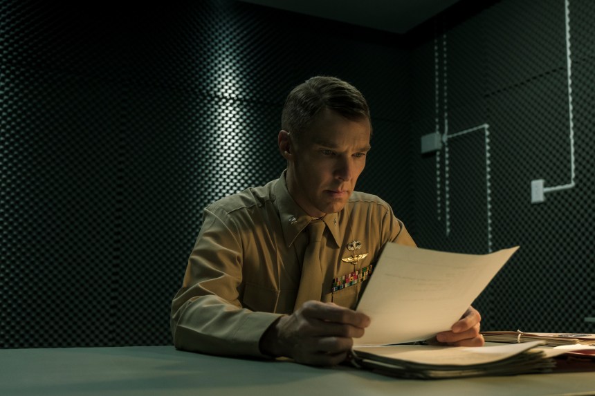 A soldier is sat in a dark room looking intensely at a piece of paper.
