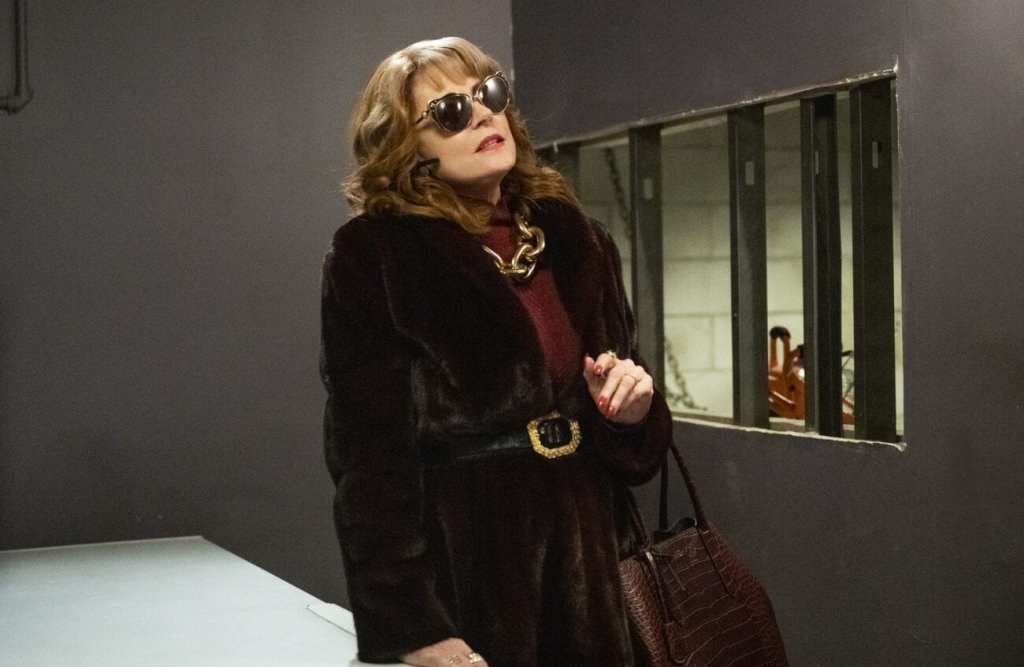 A woman wearing a fur coat and sunglasses indoors is standing in what appears to be a basement.