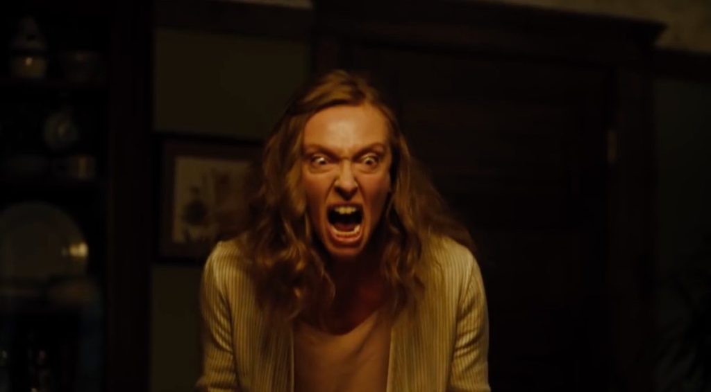 Toni Collette as Alice Graham in Hereditary (2018). Alice screams in a dimly lit room, where she is the only focus.
