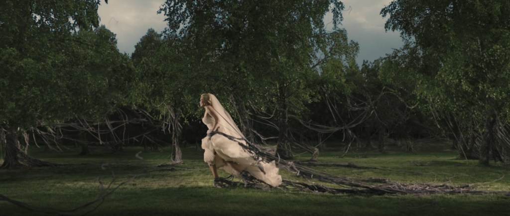 Justine trudges through a forest wearing a wedding dress. As she walks, black vines hold her back.