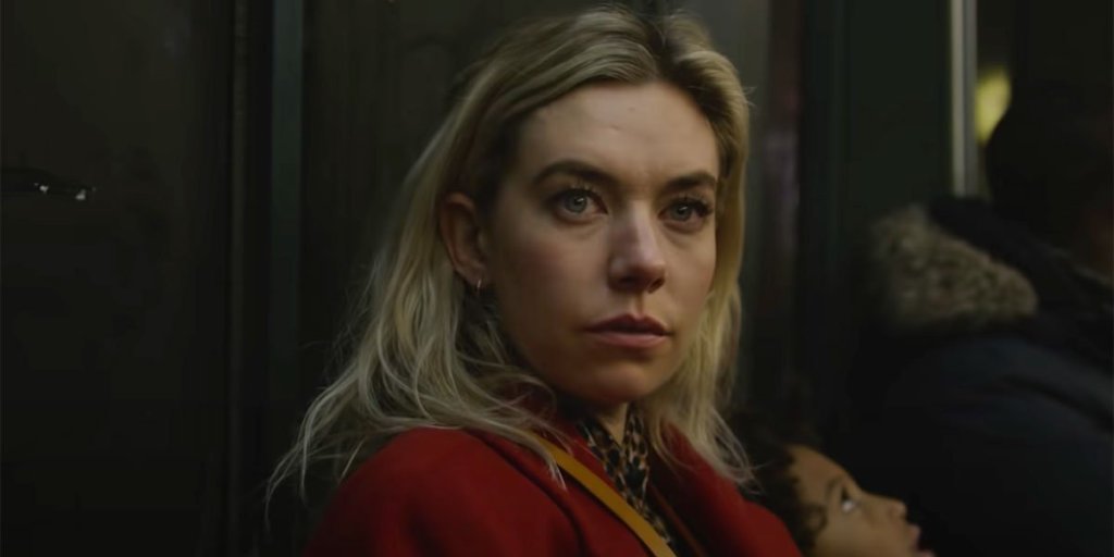 Image is from the film 'Pieces of a Woman' (2020). A blonde woman wearing a red coat sits in a subway carriage. She is looking at something in front of her.