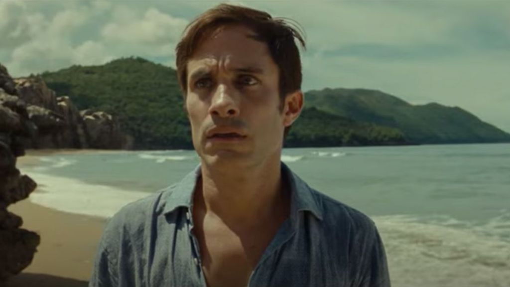 A middle-aged man with short dark hair on a beach, seen from the chest up and wearing a blue collared shirt. He has a concerned look on his face.