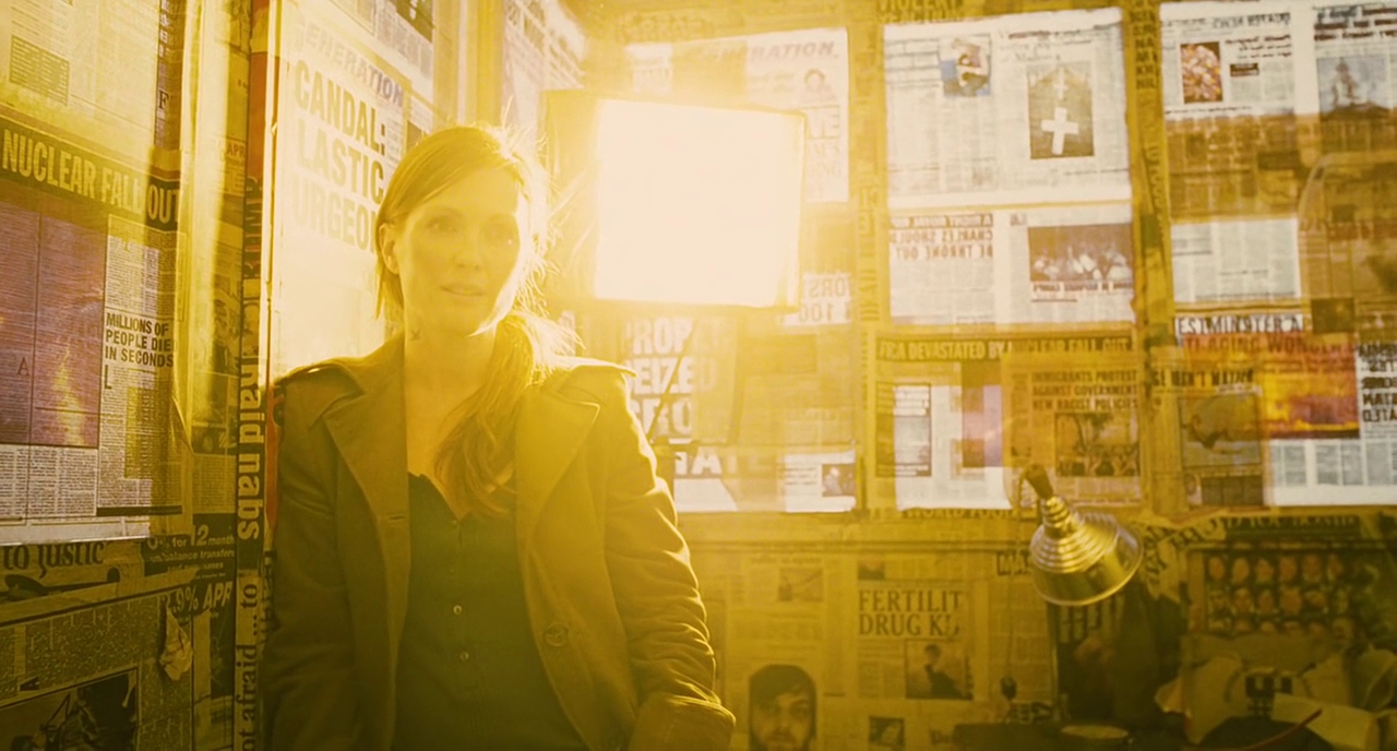 Julianne Moore as Julian in 'Children of Men' stands in front of a newspapered window. A yellow lamp illuminates her from behind.