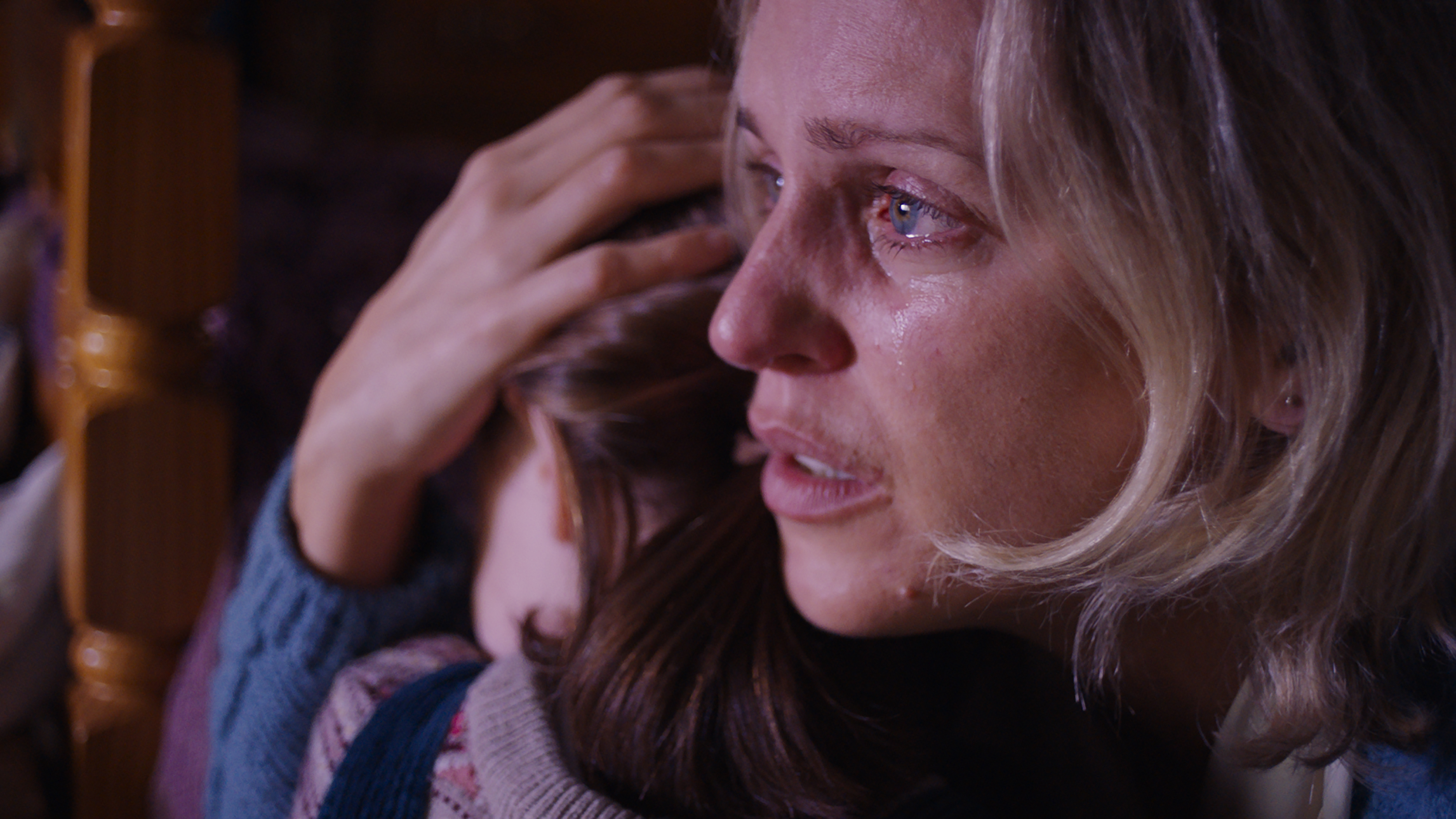 A blonde woman crying in close-up. She holds a young brunette girl close, with a protective