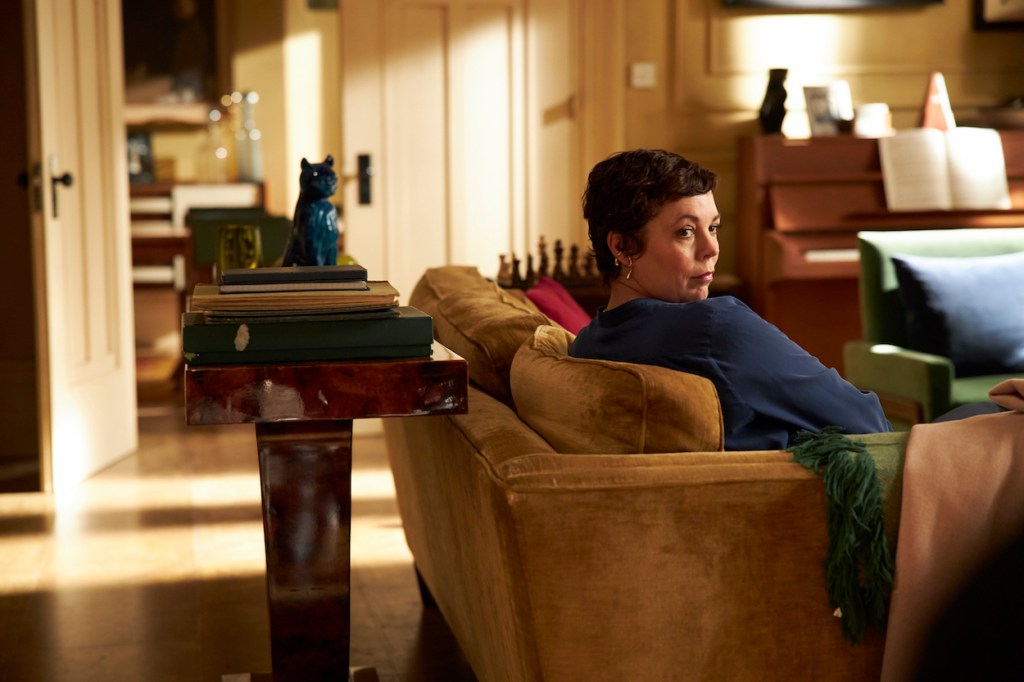 Anne, portrayed by Olivia Colman, sitting on the couch in the living room.